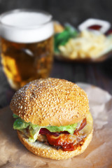 Big tasty hamburger on a paper with light beer in glass mug, close up