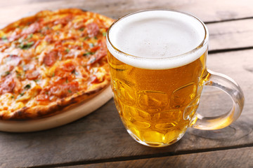 Tasty pizza and glass of beer are on wooden table, close up