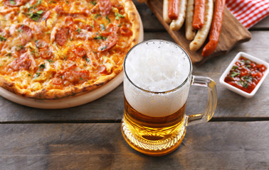 Grilled sausages, delicious pizza and glass of beer on wooden table, close up