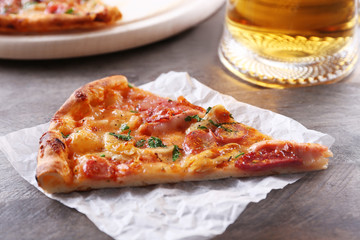 Piece of tasty pizza and glass of beer are on wooden table, close up