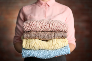 Stack of knitted clothes in female hands on blurred wall background