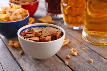 Mugs of beer and bowls with snacks on wooden table
