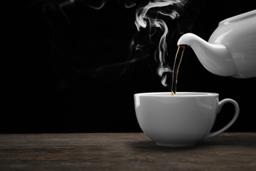 Verser du thé chaud d& 39 une bouilloire dans une tasse sur fond noir, gros plan