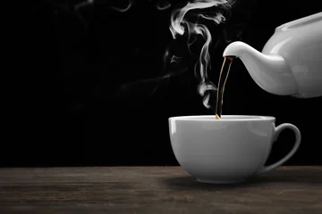 Papier Peint photo Lavable Theé Verser du thé chaud d& 39 une bouilloire dans une tasse sur fond noir, gros plan