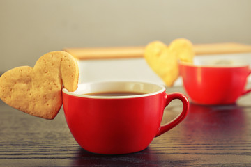 Heart shape cookie on cup of coffee on wooden table closeup
