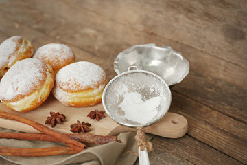 Delicious sugary donuts with spices on wooden background
