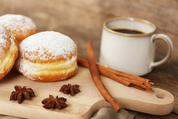 Delicious sugary donuts with spices and cup of coffee on wooden cutting board closeup