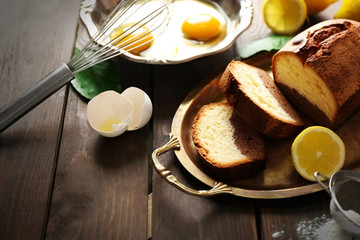 Delicious sweet cake bread in metal tray with lemons on wooden table closeup