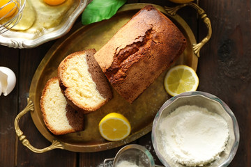 Delicious sweet cake bread in metal tray with lemons on wooden table, top view
