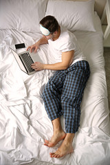 Young man lying in bed with laptop at home
