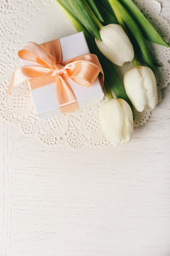 Bouquet of fresh tulips and present box on wooden table, top view