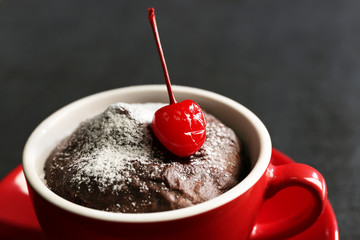 Chocolate cake in a red mug with a cherry on a wooden background, close up