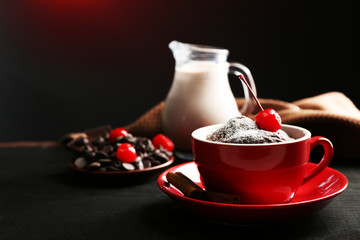 Chocolate cake in a red mug with a cherry on a black background, close up