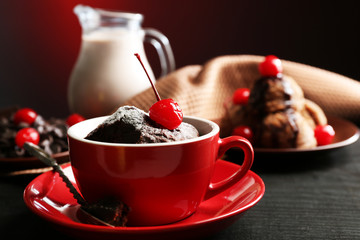 Chocolate cake in a red mug with a cherry on a dark background, close up
