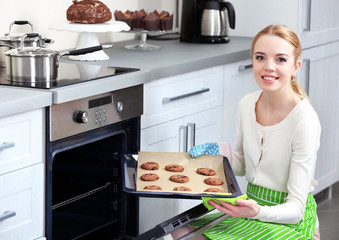 Young woman removing cookie tray from the oven in a kitchen