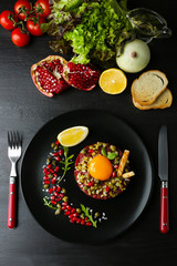 Beef tartare served in a round black plate on a dark desk, top view