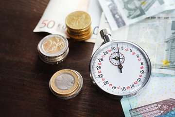 Stopwatch with euro banknotes and coins on wooden background. Time is money concept