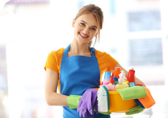 Cleaning concept. Young woman holds plastic basin with washing fluids and rags in hands
