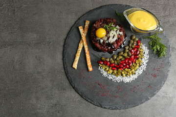 Delicious beef tartare with ingredients on dark background