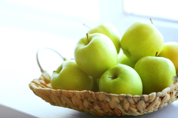 Ripe green apples in a wicker basket on windowsill