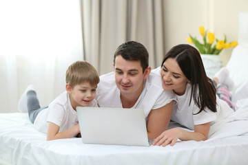 Fototapeta premium Family with laptop lying in bed
