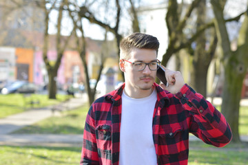 Outdoor portrait of modern young man with mobile phone in park