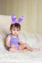 the child sits on the carpet in the purple Bunny suit