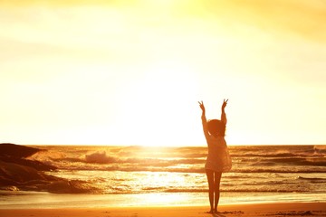 Woman standing at beach with arms raised and peace sign