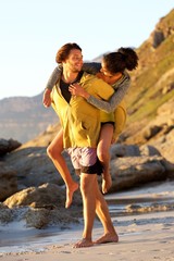 Young man carrying woman on his back at the beach