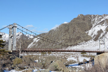 Suspension bridge Oroktoysky through the frozen Katun  river among mountains, Altai, Russia
