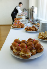 Catering banquet table with baked food snacks, cakes, coffee, open buffet dinner, waitress hands serving food at the background