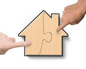 Fototapeta na wymiar Two hands assembling wooden house shape puzzles