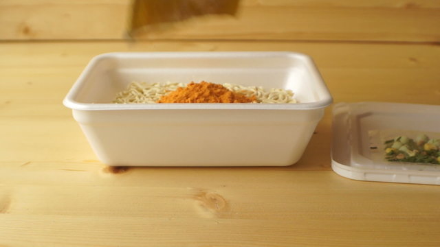 Female hands spilling bright orange seasoning in instant noodles