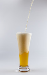 Pouring process of lager beer into a beer glass, splashes, drops and froth around glass