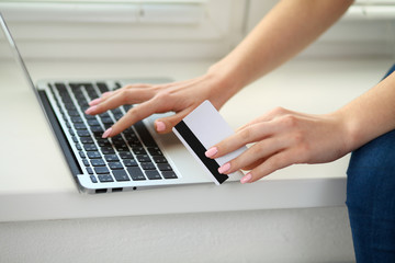 Fototapeta na wymiar Happy woman doing online shopping at home . Close- up of a hand holding a credit card next to a laptop