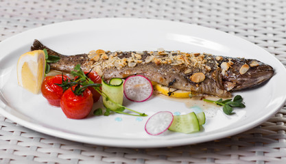 baked fish with lemon on a white plate with cherry tomatoes