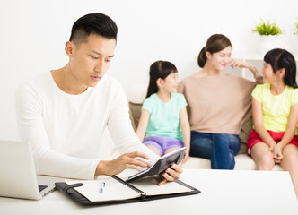 husband calculating  bills while  family  sitting on the sofa