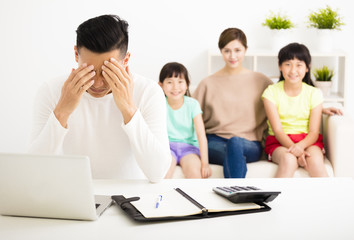 Fototapeta premium stress man calculating bills while family sitting on the sofa