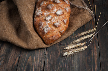 Homemade bread and ripe ears of rye on a wooden background, place for text