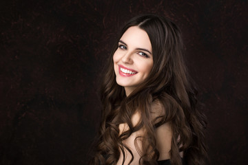 Obraz premium Portrait of a beautiful young woman with healthy long hair and beautiful smile on a dark background.