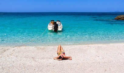 Fototapeta na wymiar Frau liegt am Sandstrand mit türkisem Meer in Griechenland