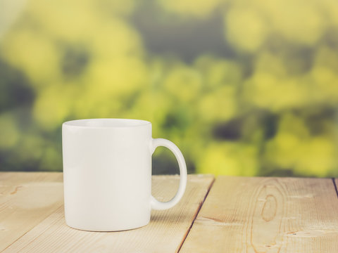Coffee cup on wood table with blurred green bokeh; vintage color filtered