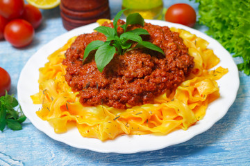 Traditional Italian pasta Bolognese or Bolognese with cooked pasta noodles topped with a spicy tomato based meat sauce garnished with fresh basil on a wooden background