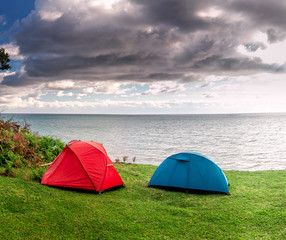 Red and blue tents are set on the grass by the sea