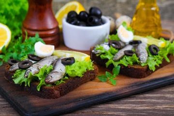 Traditional Spanish sandwiches with anchovies, lettuce and lemon on a wooden background