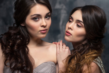 Fashion beauty portrait of gorgeous young twins women with long curly hair in luxury evening dresses