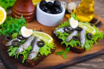 Fototapeta na wymiar Traditional Spanish sandwiches with anchovies, lettuce and lemon on a wooden background