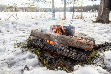 Cooking in a winter hike in the cauldron hanging over the fire in the snow-covered pine forest...