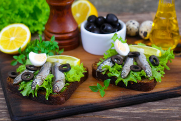 Traditional Spanish sandwiches with anchovies, lettuce and lemon on a wooden background