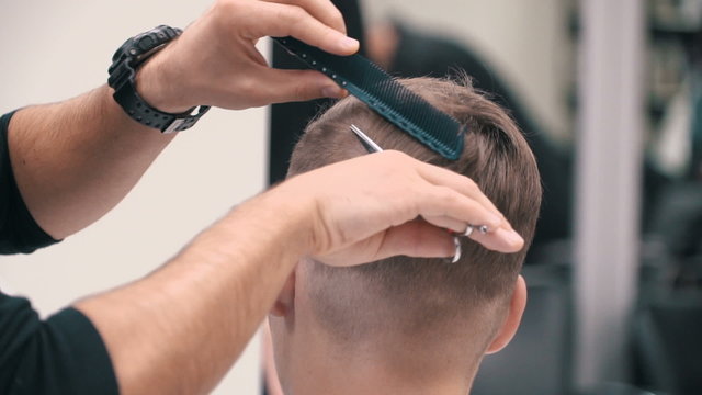 Barber cuts the hair of the client with scissors at a barber shop